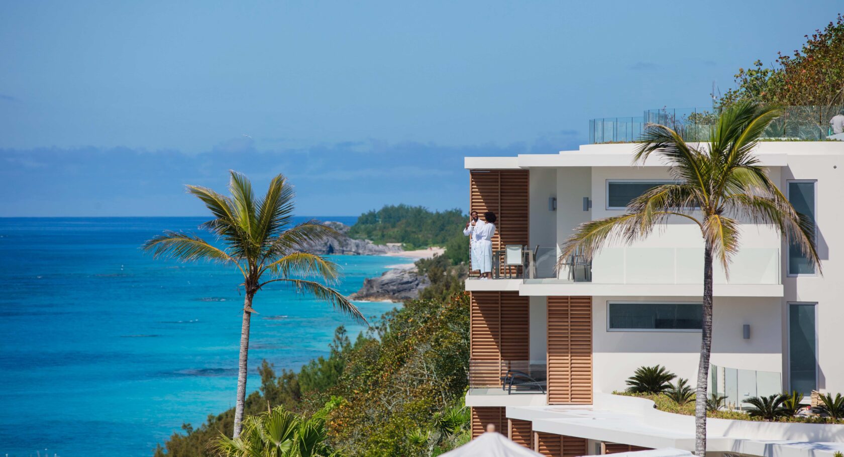 A man is standing on a balcony with a view of the ocean on his Bermuda vacation.