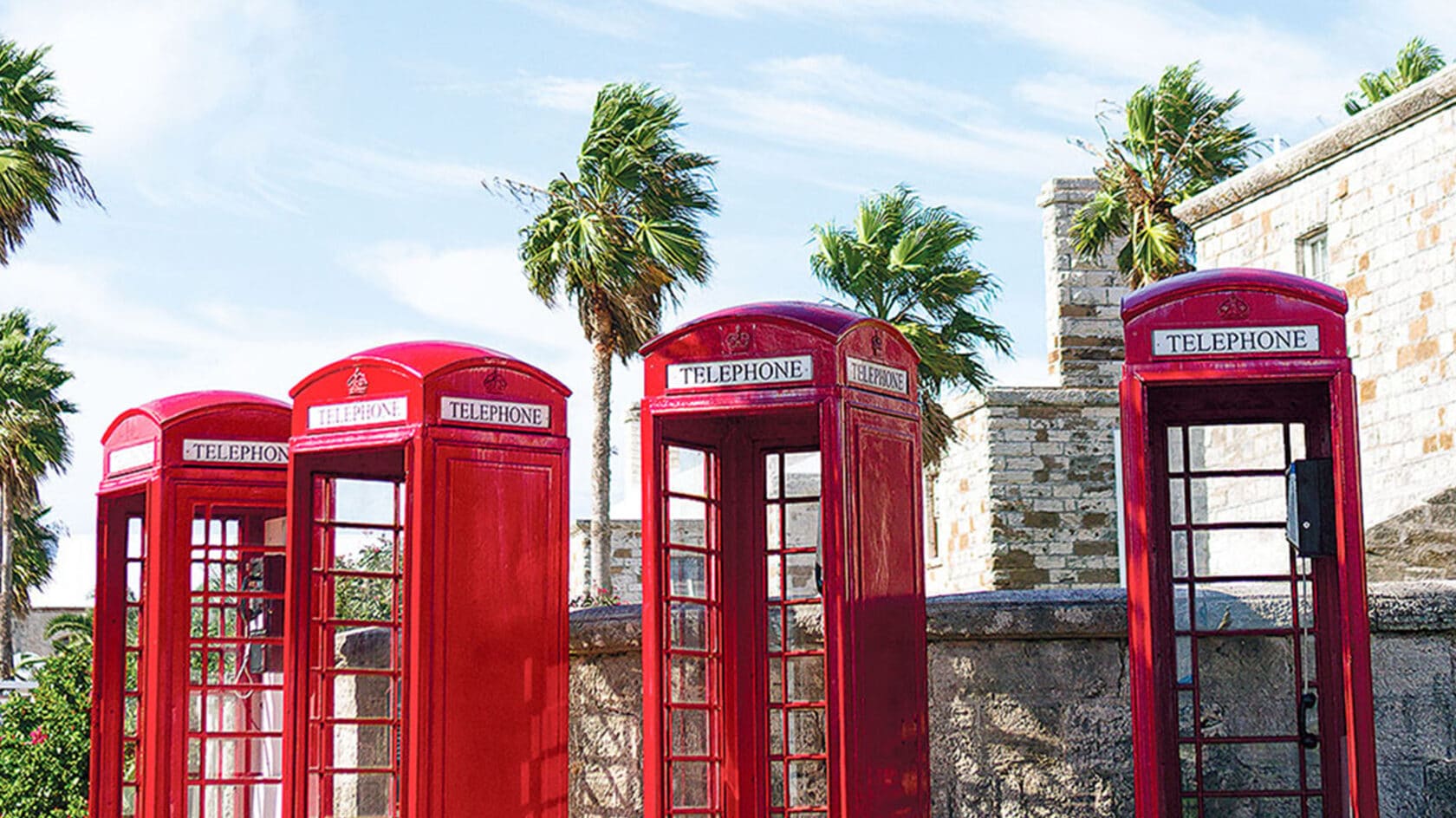 A row of red telephone booths stands in front of a stone wall.