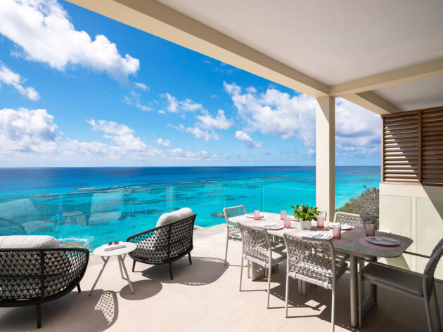 Terrace with wicker furniture and dining table overlooking a clear blue ocean under a partly cloudy sky, ideal for long-term stays near Hamilton, Bermuda.