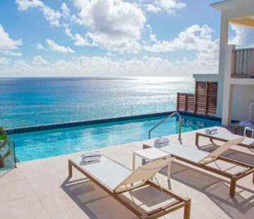 Poolside view of the ocean with two white lounge chairs on a tiled deck, surrounded by clear skies and fluffy clouds—a perfect snapshot from Bermuda vacation rentals.