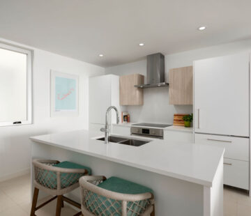 Modern kitchen in a Bermuda residence features white cabinets, an island with sink, two bar stools, stainless steel appliances, and a wall-mounted range hood. A framed picture hangs on the wall near a window—perfect for those seeking long-term stays near Hamilton.