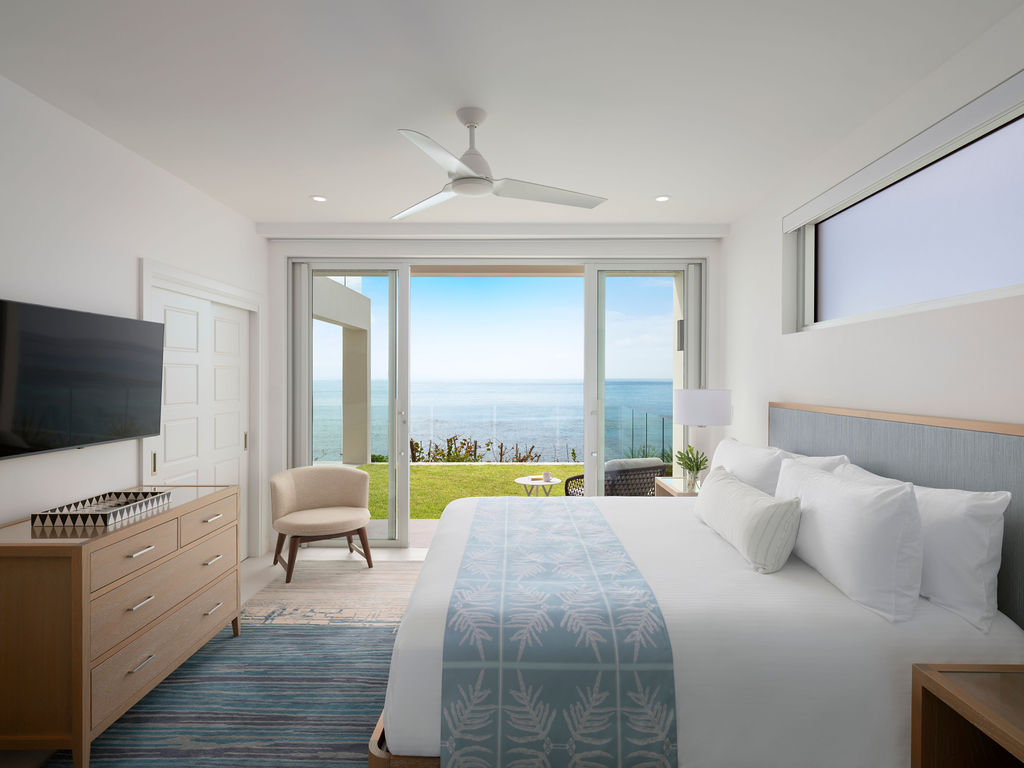 Experience luxurious living in a modern bedroom that boasts a large bed, stylish wooden furniture, and a wall-mounted TV. With breathtaking ocean views through sliding glass doors, it's the perfect spot for long-term stays near Hamilton, Bermuda.